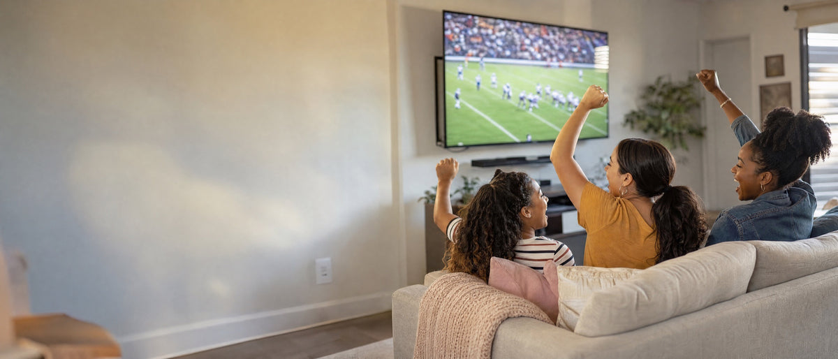 Three friends cheering on a sofa in front of a big new TV showing a football game